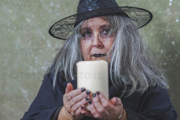 Old white-haired white-haired witch dressed in black with a hat and a large white candle in her hands