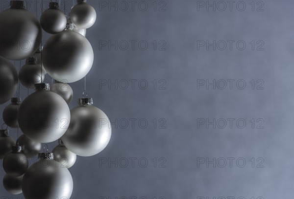 Silver Christmas balls hanged with silver thread, of a matte color, on a gray blurry backdrop, perfect as a Christmas banner or greeting card