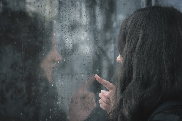 Brunette young woman and her reflection on a window covered with raindrops