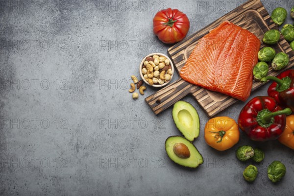 Fresh raw salmon fillet on wooden cutting board, organic bio vegetables and nuts on rustic stone grey background top view. Ingredients full of vitamins for healthy diet and nutrition, space for text, food photography, food photography