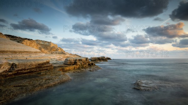 Rocky seashore seascape with wavy ocean and dramatic and beautiful sunset at sea caves coastal area in Paphos, Cyprus, Europe