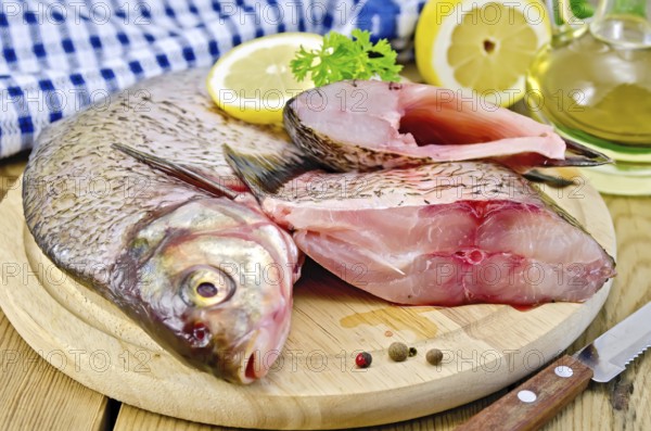 Bream whole peeled and sliced pieces on a round board, parsley, lemon, vegetable oil, napkin, knife on the background of wooden boards