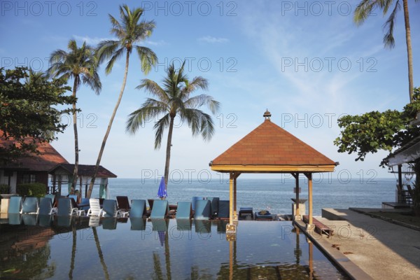 The palm tree and beach armchairs are reflected in a smooth water surface. Pool on a beach of the Thai gulf