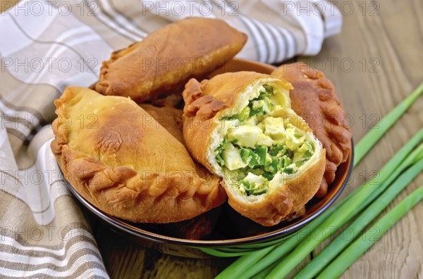 Dish with fried patties with onions and egg, napkin, a bunch of spring onions on a wooden boards background