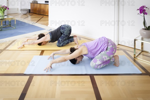 An image of two women doing yoga at home Balasana variation