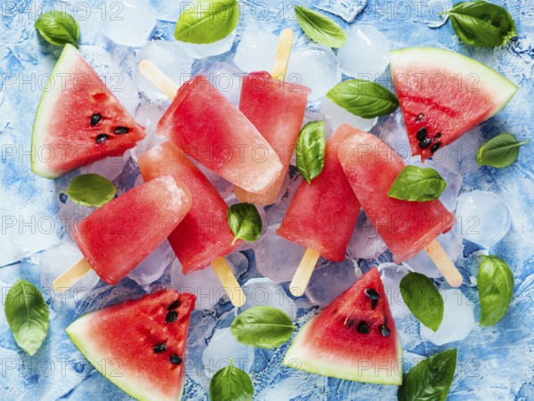 Top view of watermelon and basil popsicles on blue background with fresh green basil leaves and watermelon slices. Popsicles recipe idea