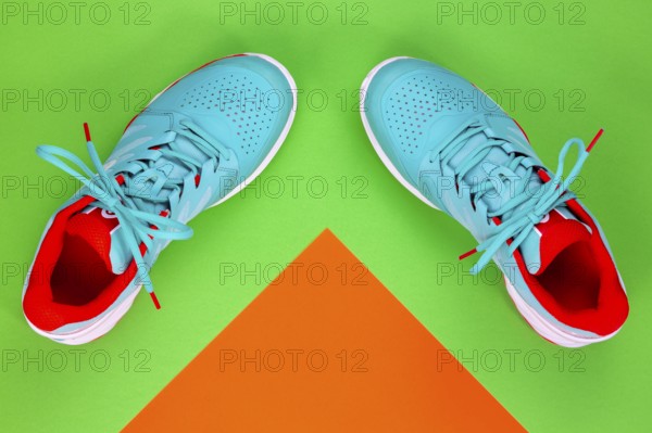 Red, cyan, white pair of new tennis shoes in studio shot over green and orange background. Directly from above