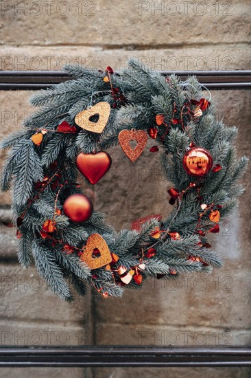 Christmas wreath of fir branches with red Christmas decorations on a stone wall.