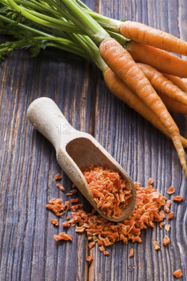 Wooden scoop with seasoning made of dried milled carrots. Tasty condiment for cooking. From above heap of fresh crisp carrots on the background