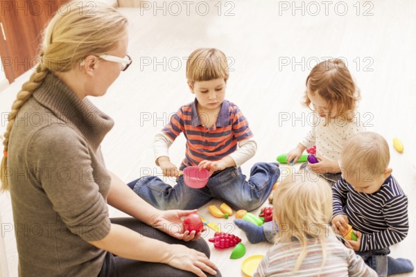 Children with teacher in kindergarten playing cooks