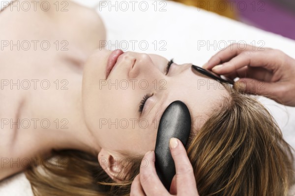 Young woman receiving facial massage with mineral stone