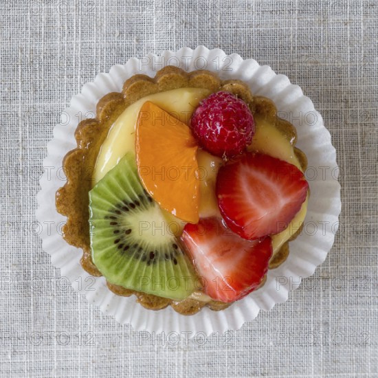 A cake with cream and mixed fruit, resting on linen tablecloth