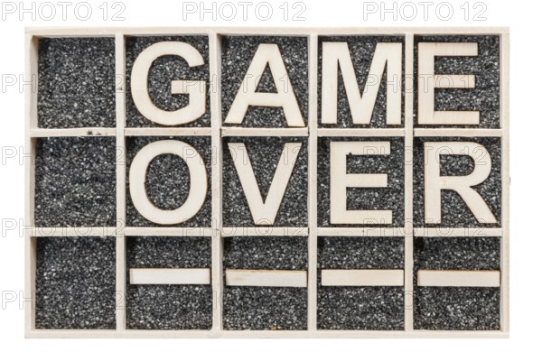 In a collecting box with black decorative sand arranged plywood letters the word GAME OVER stacked in top view on white background