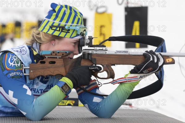 Sportswoman biathlete Anastasia Legostaeva rifle shooting in prone position. Biathlete in shooting range. Open regional youth biathlon competitions East Cup. Kamchatka, Russian Far East, Apr 12, 2019