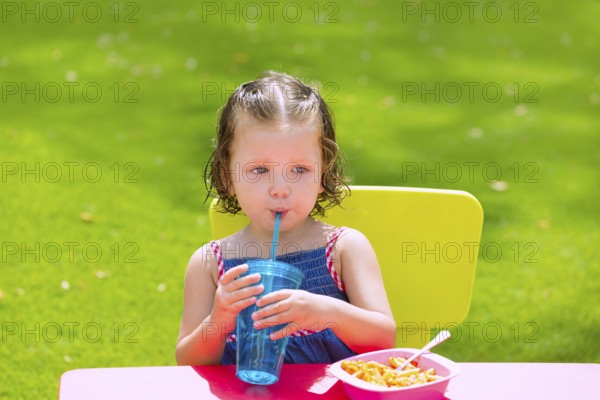 Toddler kid girl drinking eating macaroni pasta in garden turf grass outdoor