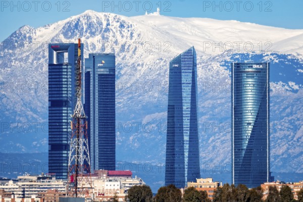 Madrid, Spain, January 12, 2022: Breathtaking view of the Spanish capital with Cuatro Torres skyscrapers, comprising of Torre Espacio, Torre de Cristal, Torre PwC, and Torre Cepsa, set against the magnificent backdrop of the snowed mountain range. Telephoto lens. Tourism and editorial projects, Europe