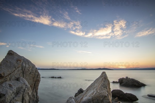 View through rocks on a sandy beach into the sunset. Landscape shot with view to the horizon over the wide sea at the coast of Ouranoupoli, Thessaloniki, Central Macedonia, Greece, Europe