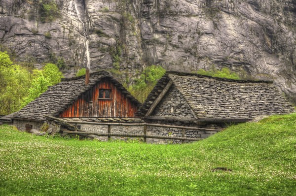 Rustic House with Stone Roof and Green Grass in Front of a Mountain wall in Ticino, Switzerland, Europe