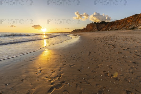 Beautiful sandy beach with red rocks and cliffs. Twilight at sunset with shallow waves on the Atlantic coast in Praia do Poço Velho, Praia da Falésia, Algarve, Portugal, Europe