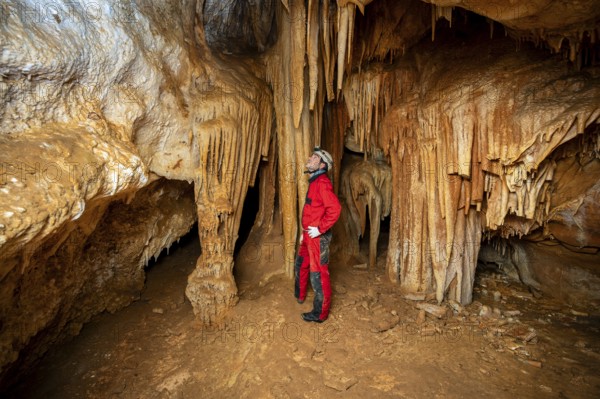 A speleologist with helmet and headlamp exploring a cave with rich stalactite and stalagmite formations. graphy