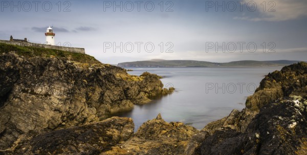 Rocky shoreline with turquoise pools and the historic Broadhaven Lighthouse on a clifftop promontory at the entrance of Broadhaven Bay
