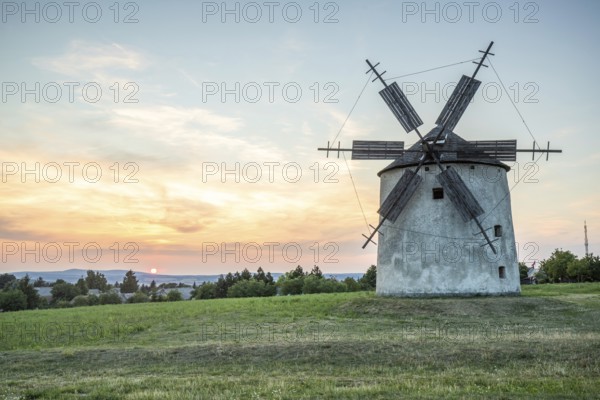 Windmill with wooden sails in a landscape with fields. Meadows and flowers appear in the sunset. Landscape shot in nature with a windmill. Historically atypical for the Balaton region in Hungary