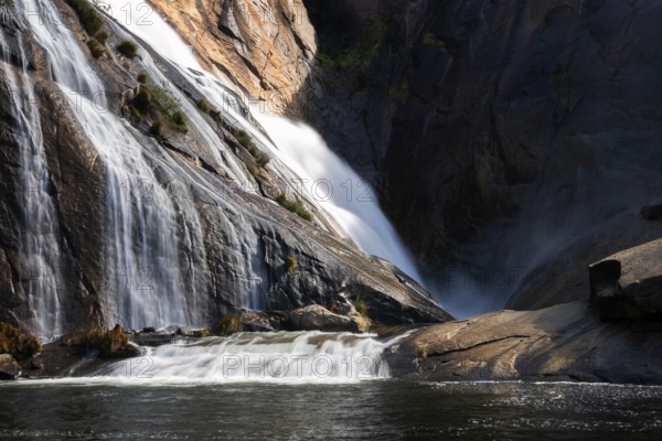 Ezaro waterfall water crashing on lake between rocks in Spain