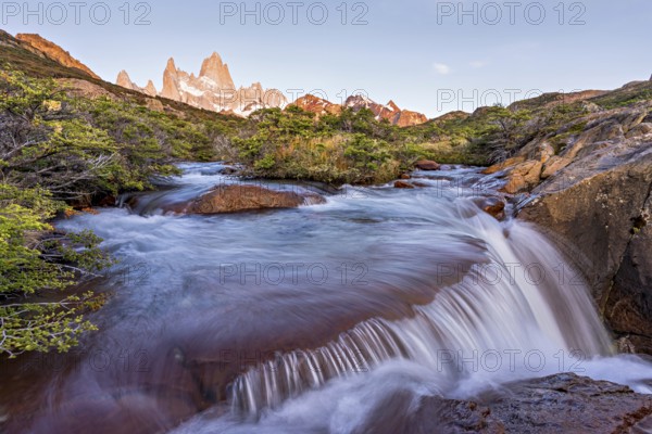A waterfall with the Fitz Roy mountain illuminated by the morning sun in the Los Glaciares National Park in Argentina