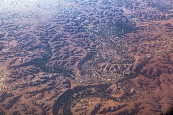 Aerial view of a vast, reddish desert landscape with river valleys and hilly areas, The dunes of the Endless Sahara from the air in Algeria