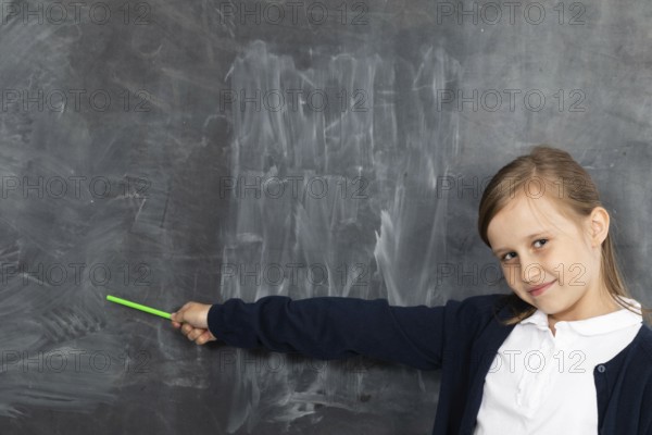 Schoolgirl shows on an empty school board. He is standing in the classroom at the chalkboard. Younger girl