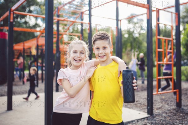 Sportive friends. Brother and sister standing together at street city gym. Children athletes hug smile during workout training. Twins boy and girl posing on playground. Physical development education