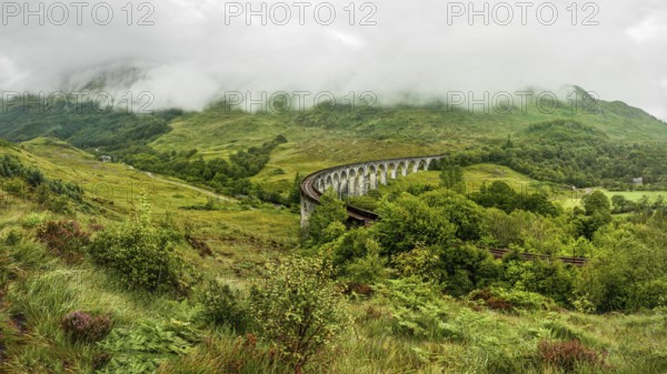 Glenfinnan railway viaduct (location from Harry Potter movie), on overcast day with grey sky and lot of green grass and trees around. Inverness, Scotland, United Kingdom, Europe