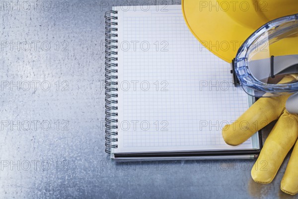 Protective spectacles gloves copybook hard hat on scratched metallic background
