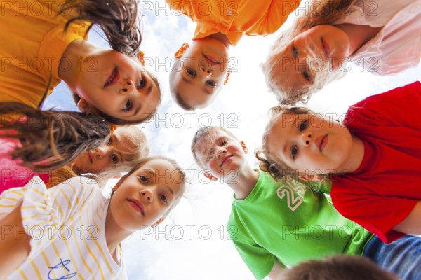 Cute girls and boys in colorful clothes standing together in circle looking at the camera on the white sky background. Summer camp togetherness