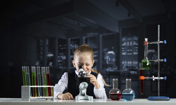 Little girl scientist looking through microscope in classroom at chemistry lesson. School chemical laboratory with glass flasks and test tubes. Schoolgirl making experiment in chemistry class