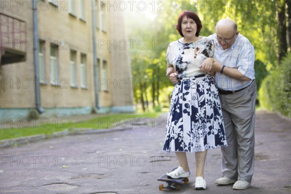Happy elderly couple with a skateboard. Handsome man and woman seniors. Husband and woman in old age for a walk in the city