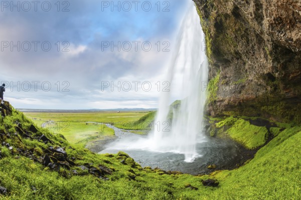 Seljalandsfoss waterfall in July. Passage under the waterfall. Photo taken fisheye lens. Warm summer day in the Arctic