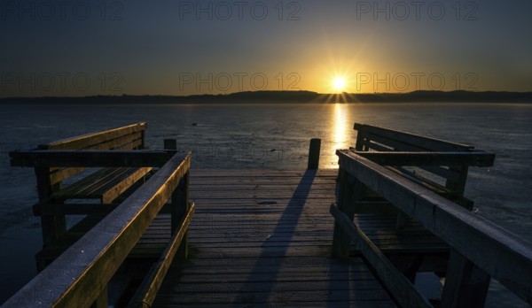 Wooden jetty with benches on a frozen lake in the light of the golden rising sun, beautiful landscape scenery, concept for a new beginning every day, copy space, selected focus