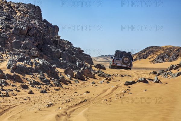 An off-road vehicle drives through a rocky desert landscape under a bright blue sky, off-road by car through the landscapes of the Sahara in Algeria