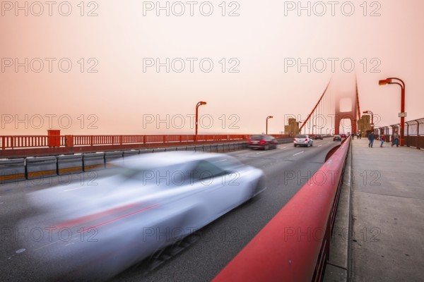 Cars crossing the San Francisco, Californian Golden Gate Bridge from the Presidio Pacific point to the north at sunset light. People along the bridge in the fog. Motion blur effect