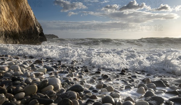 Low angle view of seascape with windy waves splashing on the rock and the sea pebbles. Rock of Aphrodite in Paphos, Cyprus, Europe