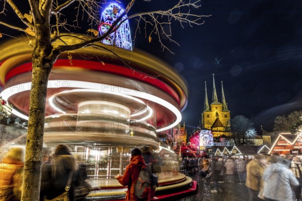Lebhafte Szene eines Weihnachtsmarktes bei Nacht mit einem Karussell in Bewegung und Kirchtürmen im Hintergrund, Erfurter Weihnachtsmarkt Erfurt