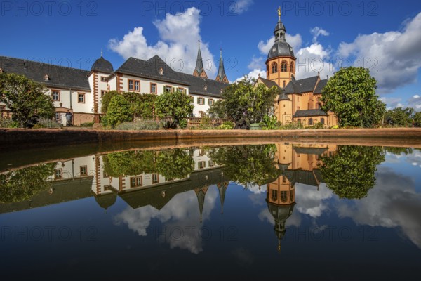 A historic monastery in the morning. Monastery walls, church and buildings are reflected in the water of a fountain. Beautiful garden in Seligenstadt Monastery, Germany, Europe