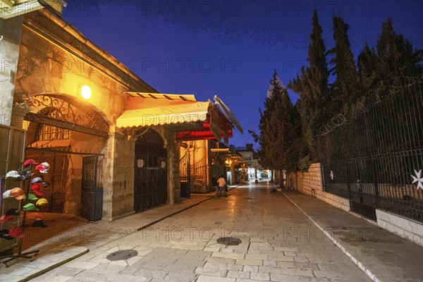 Street in Muslim Quarter in Jerusalem old city and stall .People in distance. Blue hour, twilight and moon in sky