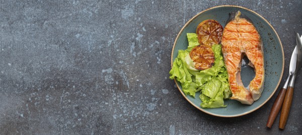 Grilled fish salmon steak and green salad with lemon on ceramic plate on rustic blue stone background top view, balanced diet or healthy nutrition meal with salmon and veggies, food photography, food photography