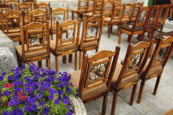 Wooden chairs with patterns on the backs stand in rows on paving stones.