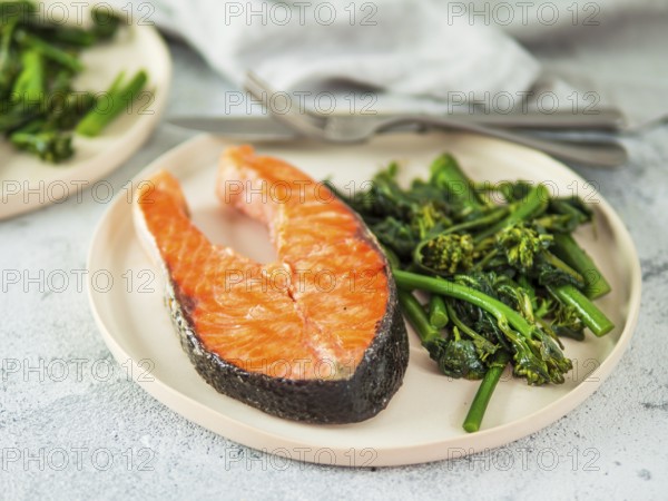 Ready-to-eat grilled salmon steak and greens - baby broccoli or broccolini and spinach on rustic craft plate over gray background. Keto diet dish