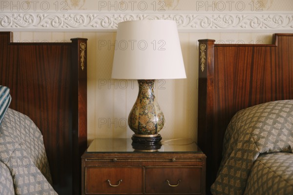 Bedside lamp on the nightstand. Refined and rich interior. Wooden bedside table next to two beds.