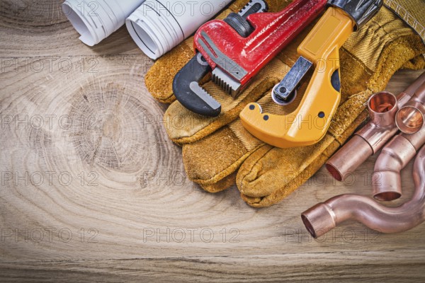Construction drawings protective gloves monkey wrench pipe cutter fixtures on wooden board plumbing concept