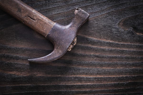 Rusty metal claw hammer on vintage dark wooden board top view construction concept